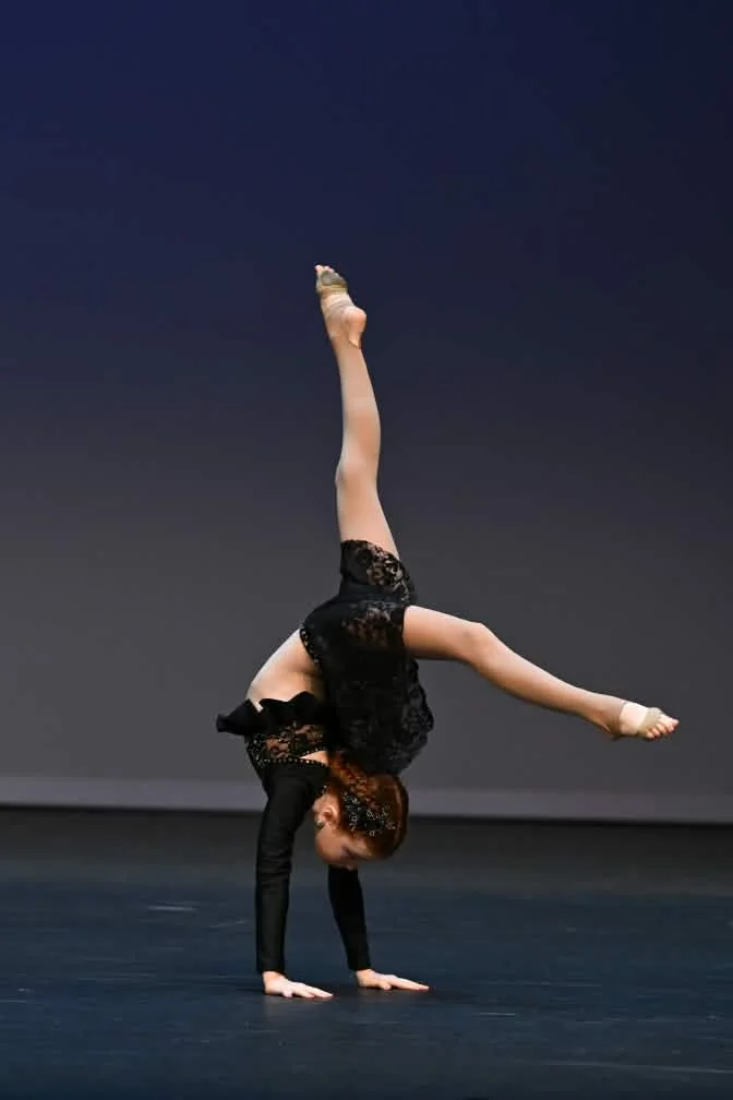 JMDS soloist in black lace holding a one-handed walkover on stage