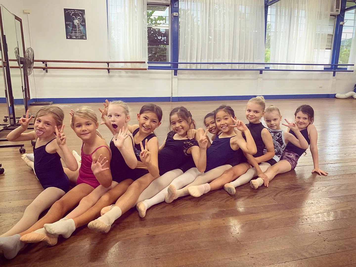 Young JMDS dancers in leotards and ballet shoes sitting together on the studio floor