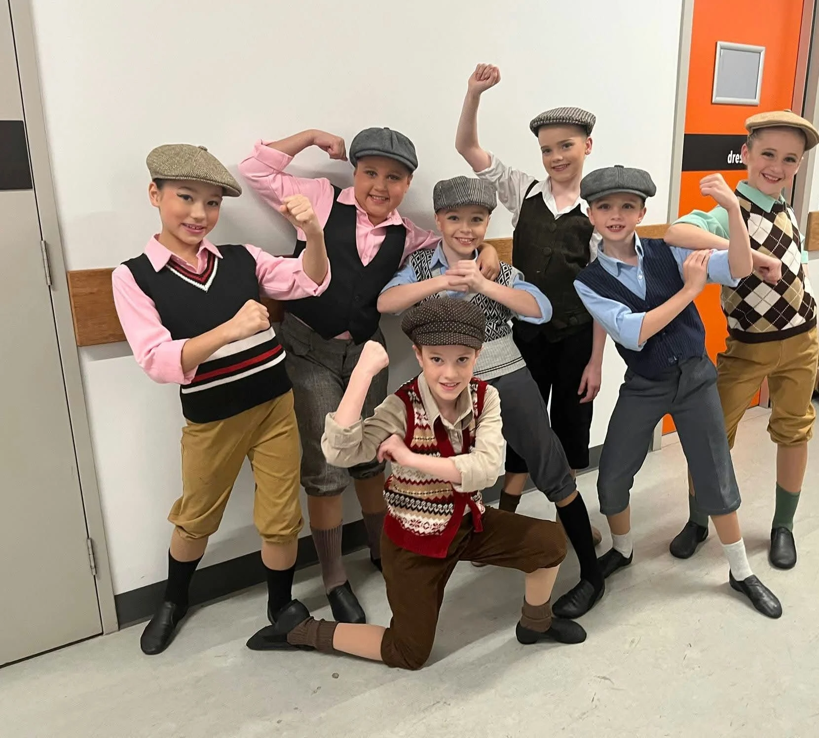 JMDS dancers in newsboy caps and vests, flexing backstage